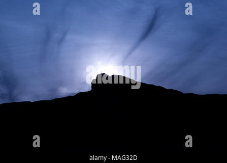 Sun glowing behind a summit cross. Mountain silhouette against dark blue sky. Egypt Stock Photo