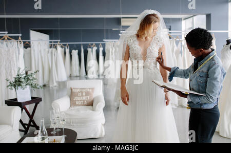 Dress designer fitting bridal gown to woman in boutique. Women checking and making adjustment to wedding gown in professional fashion designer studio. Stock Photo