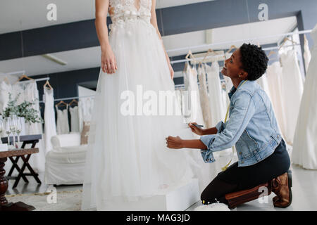 Woman making adjustment to bridal gown in wedding fashion store. Bride in her wedding dress with female dress designer making final adjustments on dre Stock Photo