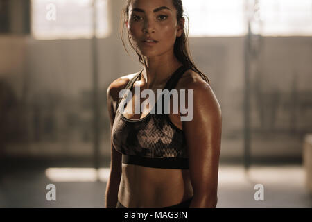 Strong and determined female in sportswear standing in the gym and looking at camera. Sportswoman after intense crossing training workout session in g Stock Photo