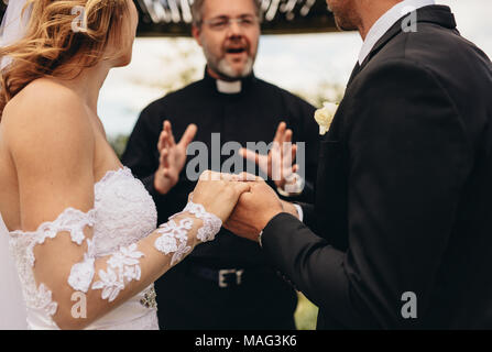 Cropped shot of couple holding hands and exchanging vows on their wedding day. Bride and groom getting married in front of a priest. Stock Photo
