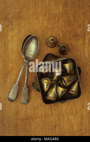 Tin containing brass and tin cake icing decorating nozzles lying on chopping board with two teaspoons Stock Photo