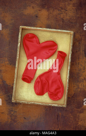 Two flat red party balloons which inflate to give heart shape lying in cardboard box Stock Photo