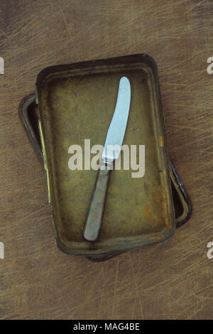 Small butter or fruit knife with marbled handle lying in brass tin on wooden chopping board Stock Photo