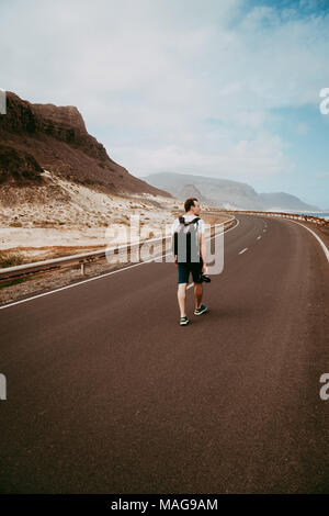 Traveler walks in the center of an epic winding road. Huge volcanic mountains in the distance behind him. Sao Vicente Cape Verde Stock Photo