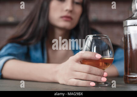 Young female alcoholic social problems sitting at table holding glass with whiskey close-up looking upset Stock Photo