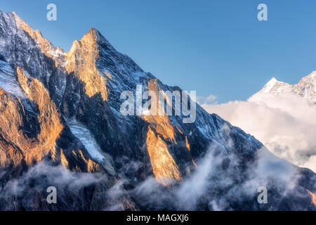 Majestical scene with mountains with sunlit peaks in clouds in Nepal. Landscape with beautiful high rocks and blue sky in sunny bright day. Nature bac Stock Photo