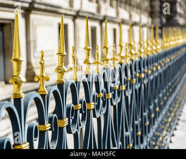 A heavy black wrought iron fence topped with golden spikes and fleur-de-lis running along a historic building in Paris, France. Stock Photo