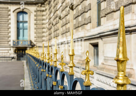 A heavy black wrought iron fence topped with golden spikes and fleur-de-lis running along a historic building in Paris, France. Stock Photo