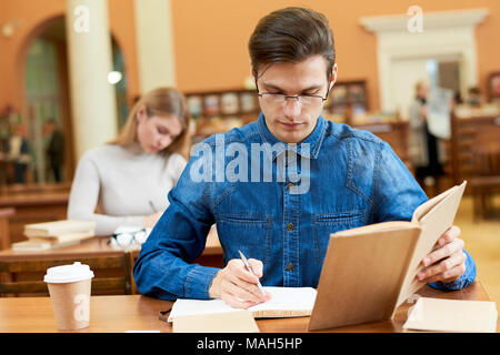Concentrated geek taking notes in library Stock Photo