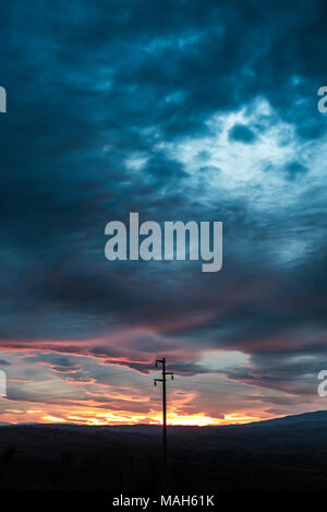 Power line - Single column in front of dramatic sky at sunset, near twilight Stock Photo
