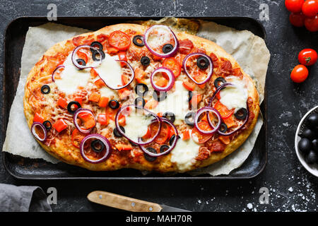 Homemade pizza with black olives, onion, tomato sauce, pepper and cheese on baking sheet. Top view Stock Photo