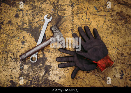 Gloves, hammer and wrench on old metal background, top view, closeup. Stock Photo