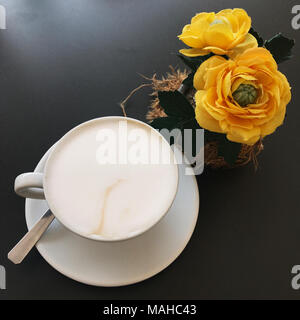 Cup of cappuccino coffee on a black table with yellow roses Stock Photo