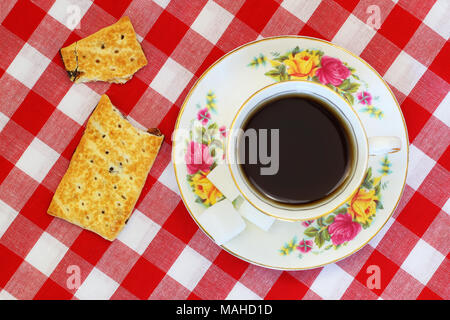 Cup of tea in vintage cup and sweet cracker broken in half on red and white checkered cloth Stock Photo