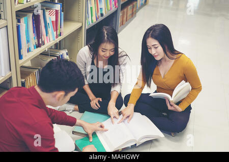 Group of happy students with books talking and preparing to exam in library. Education concept. Stock Photo