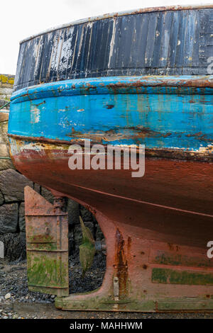 the hull and keel of an old fishing trawler in the harbour at newlyn in cornwall with the rusty and corroded propellor and rudder exposed on the mud. Stock Photo