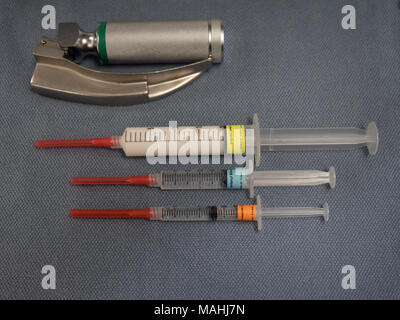 Three syringes with sedatives for anesthesia, propofol, fentanyl and midazolam, along with a laryngoscope with MacIntosh blade on a blue gray towel. Stock Photo