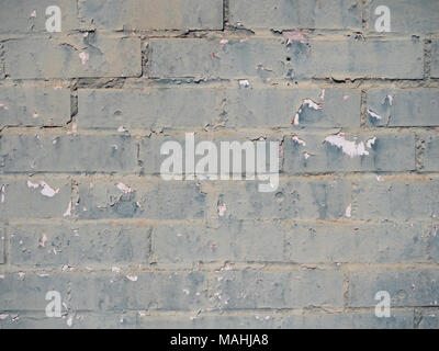 Close up of rectangular brick wall painted green or celadon. The old wall's paint is worn and chipping, exposing white paint underneath. Stock Photo