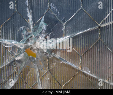 Close up of a bullet hole through wire mesh glass. The glass has ridges and the bullet hole caused rays of cracks in the window. Stock Photo