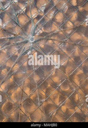 A bullet hole through wire mesh glass with glass breaks in a star pattern. Stock Photo