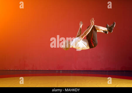 A young athletic man in sportswear makes a somersault in the wrestling hall. Parkour in the gym Stock Photo