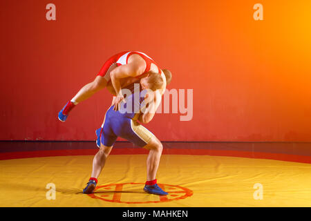 Two strong men in blue and red wrestling tights are wrestlng and making a suplex  wrestling on a yellow wrestling carpet in the gym. Wrestlers doing g Stock  Photo - Alamy