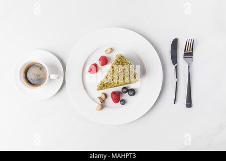 top view of sweet cake with pistachios and berries on plate and cup of coffee isolated on white Stock Photo