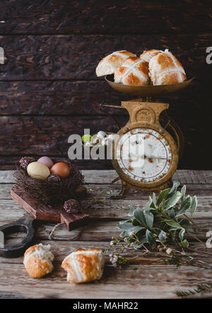 Scales with hot cross buns on table with flowers and chicken eggs Stock Photo