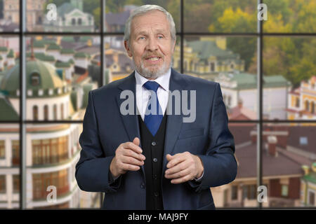 Old european politician man portrait. Senior man in suit talking, checkered windows background with view on small european town. Stock Photo