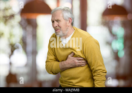 Elderly old man with discomfort in chest. Older man having chest pain, blurred restaurant background. Stock Photo