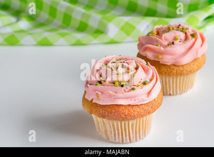 Two pink rose swirled frosted cup cakes with pistachio nut sprinkles on white background with space for your text Stock Photo