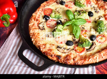 Fresh pizza in a pizza pan. Vegetarian pizza or vegetable pizza with broccoli, tomatoes, mushrooms, olives and cheese. Cheesy pizza, homemade pizza. Stock Photo