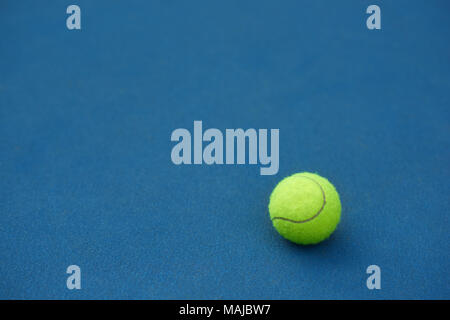 Yellow bright tennis ball is lying on on blue carpet. Made for playing tennis. Contrast image with satureted colors. Blue tennis court. Stock Photo