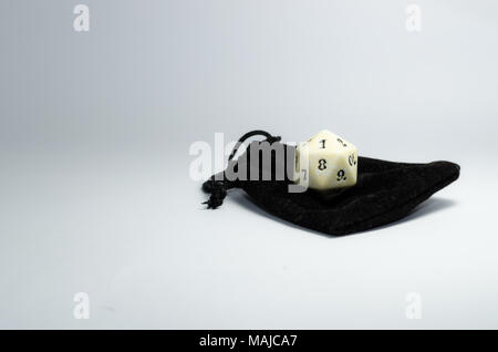 white twenty-sided dice on a small black purse on a white background. Dice of role playing game Stock Photo
