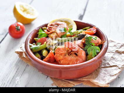 Fresh tapas plate with shrimps and green asparagus, lemon slice and parsley. Gourmet dish on a white wooden table. Stock Photo