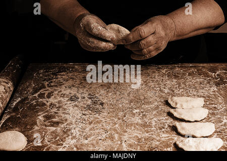 The hands of an old grandmother mold vareniks on a dark background 2018 Stock Photo