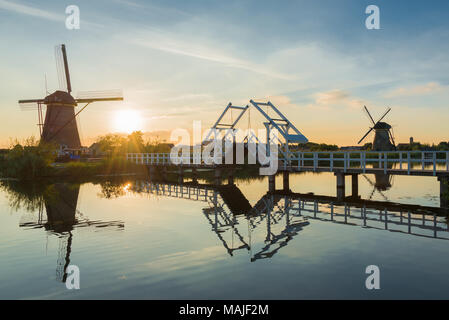 A landscape in the Netherlands with two windmills and a drawbridge in the low sun at sunset with reflection in the water in Kinderdijk, Netherlands. Stock Photo