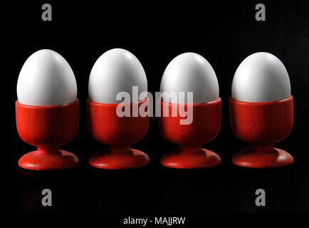 four eggs in red cups on black background Stock Photo
