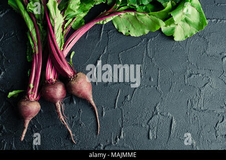 Pile of homegrown organic young beets with green leaves on dark stone table. Fresh harvested beetroots on black concrete background with place for tex Stock Photo