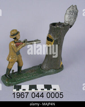 Cast iron mechanical bank depicting Teddy Roosevelt hunting. To operate the bank, a coin is placed on the barrel of the gun and the lever between Teddy's feet is pressed causing the coin to be shot into a hole in the tree as bear's head pops out of the tree top. Manufactured by the J and E Stevens Company circa 1907. Title: Teddy And The Bear Mechanical Coin Bank  . circa 1907. Charles A. Bailey (Designer), J and E Stevens Company (Maker), Stock Photo