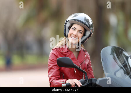 Happy biker wearing helmet sitting on a motorbike dreaming looking above on the street Stock Photo