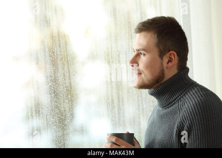 Happy man looking outside through a window at home in a rainy day Stock Photo