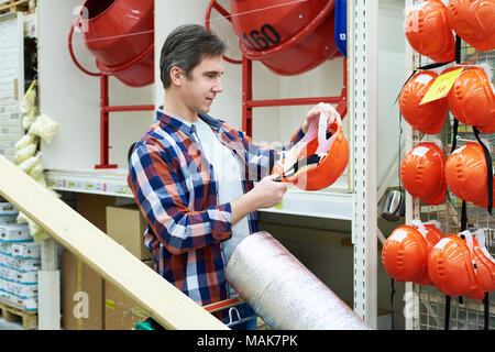 Man selects and buys a construction hard hat in a store Stock Photo