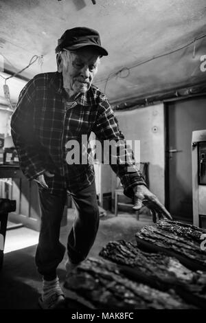 Handsome 80 plus year old senior man portrait. Black and white full body image of elderly man in boiler room, staring fire to heat house. Stock Photo