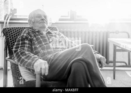 Handsome 80 plus year old senior man portrait. Black and white full body image of elderly man sitting in an armchair in a nursing home. Stock Photo