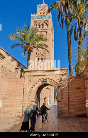 MOROCCO MARRAKECH THE KOUTOUBIA MOSQUE EARLY MORNING PEOPLE PASSING UNDER THE ARCHWAY AND PALM TREES Stock Photo