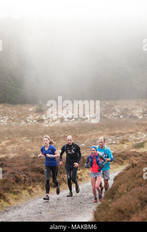 A mixed group of people running in a foggy day along a muddy path Stock Photo