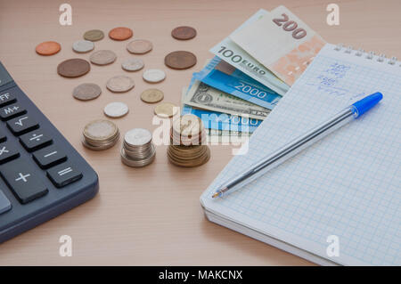 Notepad, bills, various money and a calculator on the table. Stock Photo