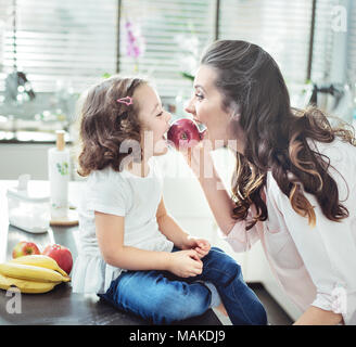 Mother and cheerful daughter biting an apple Stock Photo